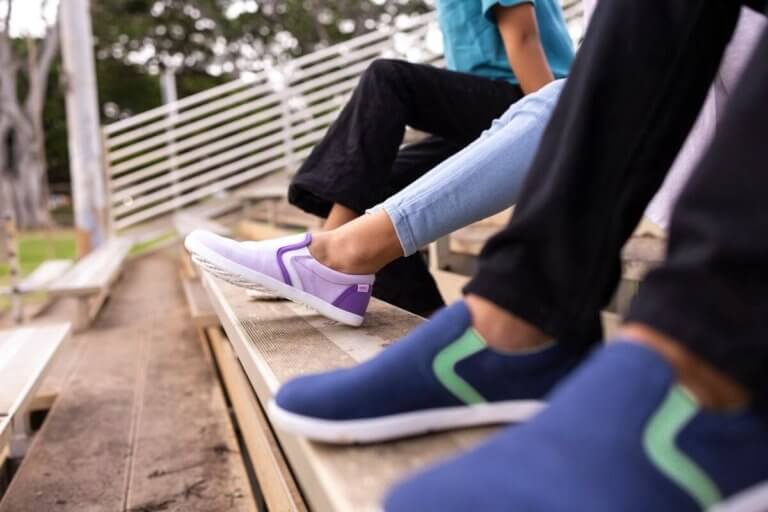 Three kids sitting on bleachers with their Dillon Canvas Slip-On Youth shoes