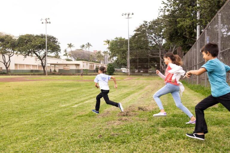 Three kids running across a grassy field in their Dillon Canvas Slip-On Youth shoes