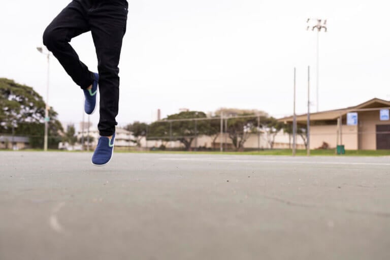 A boy jumping in the air in a basketball court in his Dillon Canvas Slip-On Youth shoes