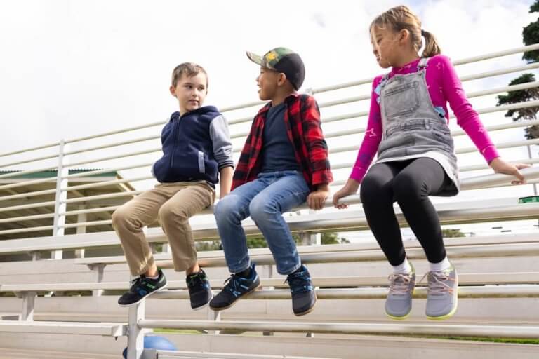 Three kids sitting on a metal fence on the bleachers with their Prio Youth shoes