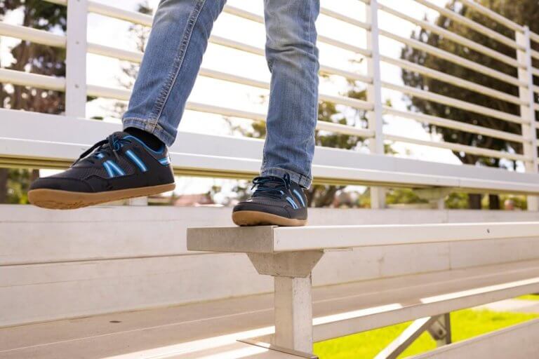 A boy balancing walking along a metal bleacher in his Prio Youth shoes