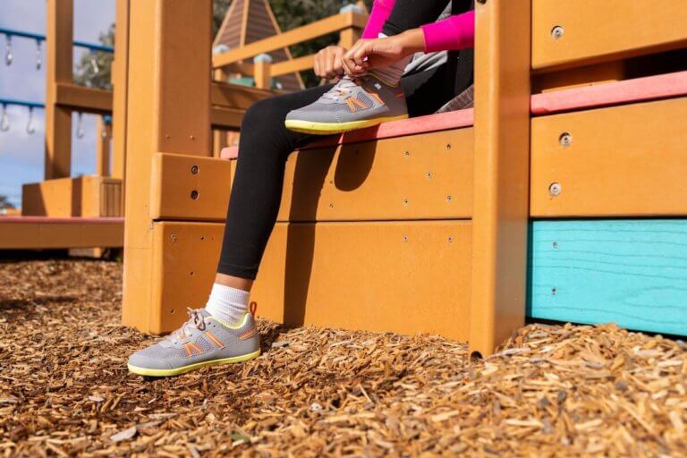 A girl tying her shoelaces on her Prio Youth shoes at a playground