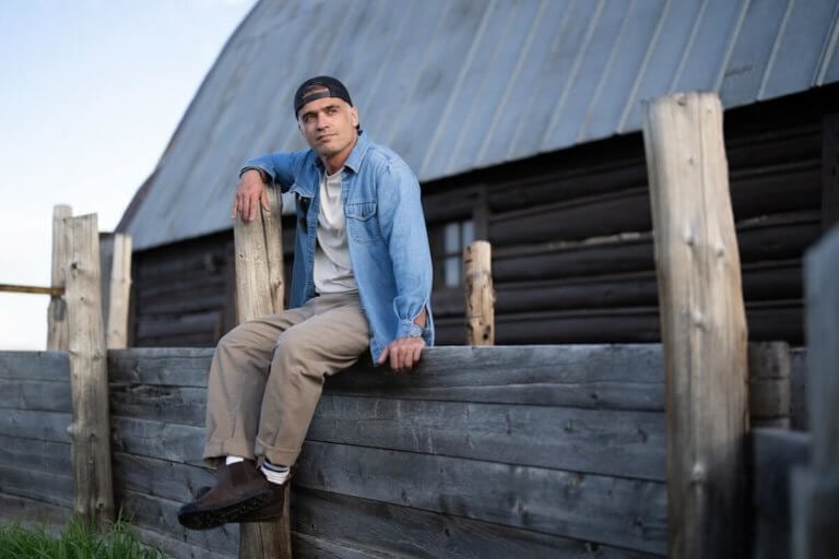 A man casually sitting on a wooden fence wearing Ridgeway Chelsea boots