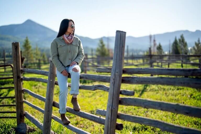 A woman casually sitting on a wooden fence wearing Ridgeway Chelsea boots with mountains and trees in the background